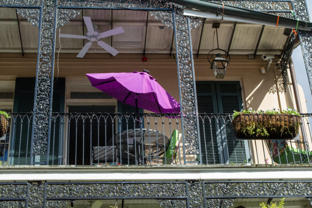 photo of a wrought-iron balcony with a bright purple umbrella unfurled on it